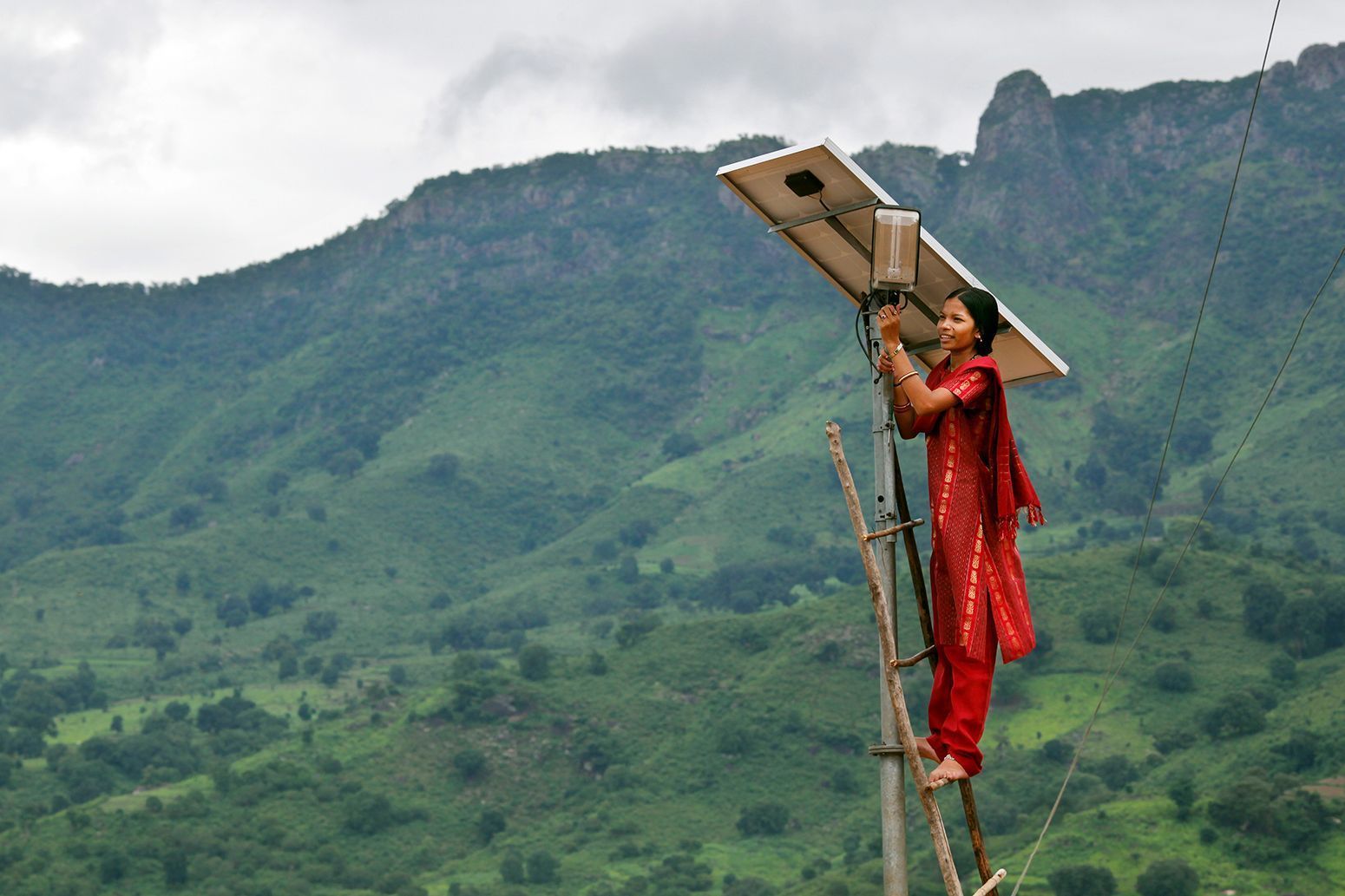 A woman with a solar panel in front of a mountain ridge - clean energy for the Global South is key to a good future for all